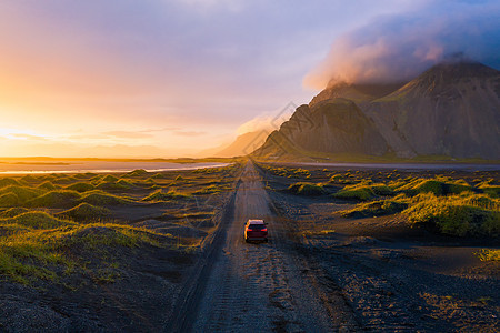 日落时的石路 与山和一辆汽车驾驶 冰岛旅游丘陵碎石阳光海滩悬崖荒野天空黑沙海洋图片