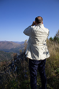 人透过望远镜向山上望去游客蓝色冒险旅行玻璃登山者运动山脉地平线顶峰图片