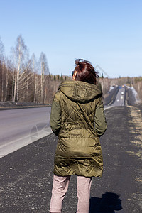 一名年轻妇女在路边走过 森林中的道路航程季节天气冒险旅行头发国家外套成人女孩图片