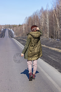 一名年轻妇女在路边走过 森林中的道路帽子成人航程天空街道天气女性季节场地头发图片