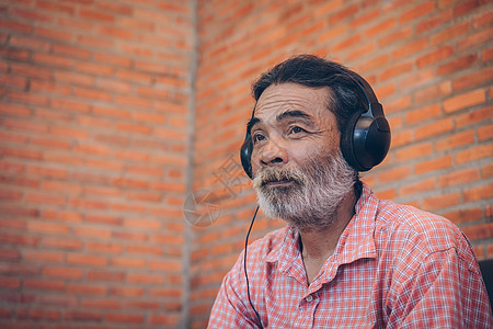老头子从耳机里听音乐的男人社会老化笔记本沉思工具公寓眼镜娱乐广告图片