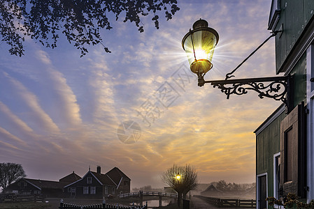 悬挂的灯柱美丽的典型荷兰木屋建筑在日出时刻反映在位于荷兰阿姆斯特丹北部的平静的运河上金属建筑学邮政灯笼天空街道城市蓝色照明路灯图片