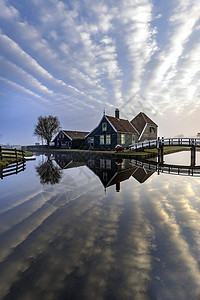 在位于荷兰阿姆斯特丹北部的镇静运河上仿照着美丽和典型的荷兰木制房屋建筑旅游森林日落木头公园历史地标蓝色反射天空图片