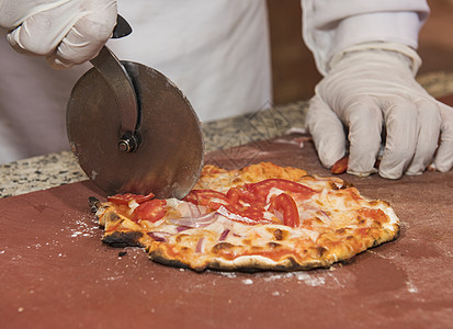 厨师用车轮切割器把比萨切成切片图片