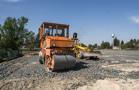 在道路建设和修复沥青路面时 用蓝色的天空在石块上架立着橙色光振动滚压机柏油压实机卡车工地车轮边缘建筑赛跑者滚筒商业图片