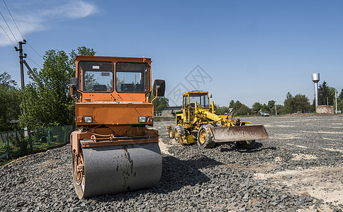 在道路建设和修复沥青路面时 用蓝色的天空在石块上架立着橙色光振动滚压机柏油压实机车轮机械建筑蒸汽碎石活动挖掘机振动器图片