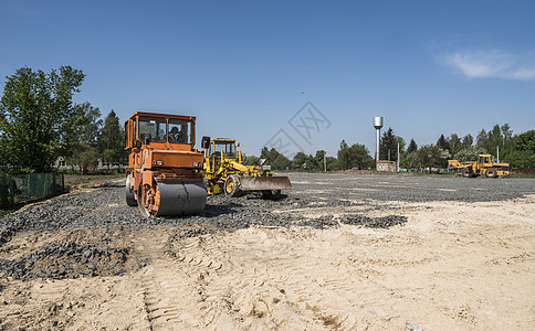 在道路建设和修复沥青路面时 用蓝色的天空在石块上架立着橙色光振动滚压机农村挖掘机装载机压实机操作员机械车辆建筑振动活动图片