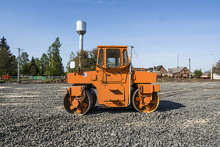 在道路建设和修复沥青路面时 用蓝色的天空在石块上架立着橙色光振动滚压机街道车道活动装载机施工柏油边缘建筑工作车辆图片