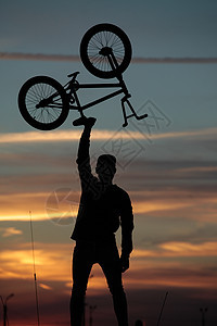 一名骑自行车的骑自行车者用脚踏在太阳下头顶着头顶运动员男人训练阳光旅行活动天空山地车小轮车日落图片