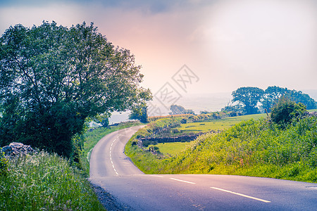 在恩加伦农村中部带干岩墙和树木的弯曲道路缠绕日落多云土地旅行太阳国家乡村曲线天空图片