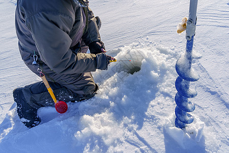 一只渔民的手 一个冬季钓鱼杆和冰上的钻井图片