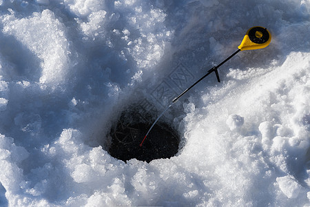 冰洞和用于冬季捕捞的钓鱼杆图片