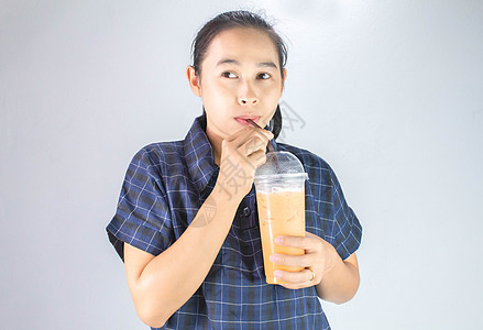 快乐的亚洲年轻女子正在喝泰茶和牛奶 在亚洲流行饮料工作室女孩稻草橙子女性食物女士咖啡店玻璃图片