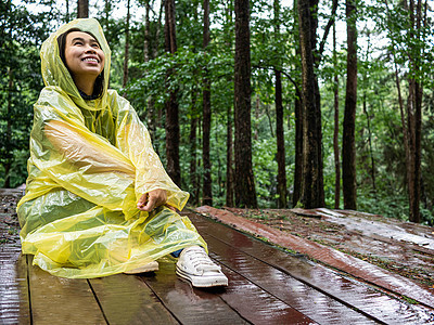 身穿黄色雨衣的亚洲快乐女人坐在木地板上图片