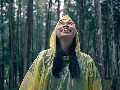 身穿黄色雨衣的亚洲快乐女性在雨中站立的肖像喜悦女孩成人天气森林雨滴花园微笑季节幸福图片