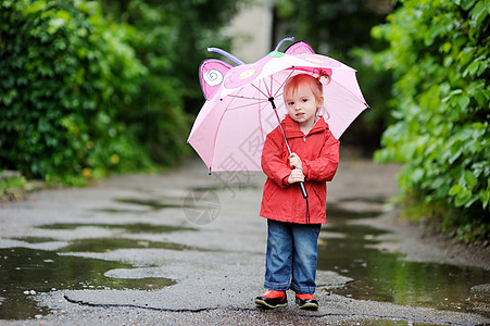 秋天下雨时的可爱小孩女孩靴子童年雨衣微笑乐趣外套天气人行道红色水坑图片