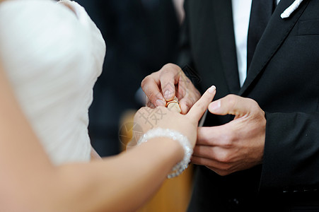 把戒指戴在新娘的手指上男性金子订婚男人白色配偶裙子蓝色庆典花束图片
