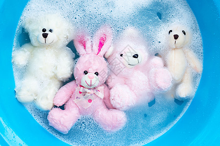洗衣洗涤水分中带玩具熊的浸泡式兔子娃娃洗涤剂蓝色衣夹衣服工作粉末机器盆地浴缸黑发图片