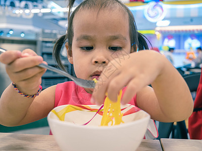 亚洲快乐的小孩在商场食品法庭吃着美味的面条 手和叉子图片