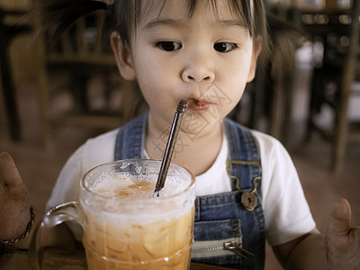 快乐的亚洲女孩在咖啡厅外面吃茶冰茶和杯装牛奶 表情真可爱玻璃孩子橙子奶油咖啡茶点童年美食女性桌子图片