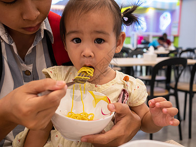 亚裔妈妈喂面给女儿吃 在商场食品法庭用叉子吃饭女性购物中心面条美食孩子食物母亲手指乐趣广场图片