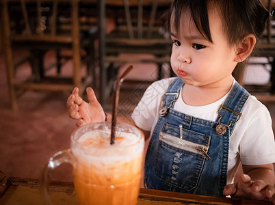 快乐的亚洲女孩在咖啡厅外面吃茶冰茶和杯装牛奶 表情真可爱冰镇茶点桌子玻璃咖啡孩子奶油食物橙子女性图片