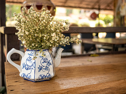 在咖啡厅的木制桌子上放着手工制作的陶瓷茶壶花瓶中的花朵图片