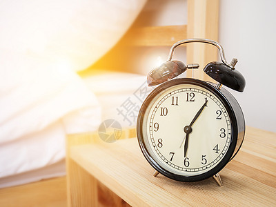 闹钟 觉醒时间概念 早上6点5分钟的雷特罗闹钟 放在木制床边桌子上 上面有白色床单和晨光背景图片
