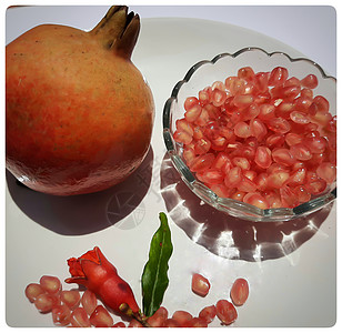 两颗石榴和石榴籽放在碗里 里面有闪亮的红色珠宝 花蕾放在碗里 漂亮地放在白盘里健康粮食叶子卡片农业浆果作品义者甜点热带图片