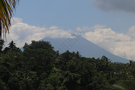 透过前方的树木观察印度尼西亚巴厘岛对面山丘上活跃的甘ung阿贡火山 Azure蓝色天空 山边有浓密的白云Azure蓝天森林荒野爬图片