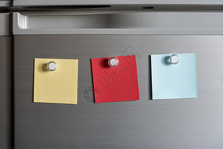 冰箱门背景上的有色磁铁粘贴纸条办公室木板商业空白邮政笔记蓝色黄色图片