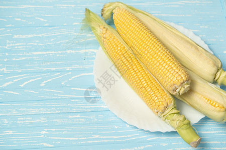 白盘蓝色背景上有绿叶的玉米鳕植物食物营养美食饮食收成谷物桌子金子农业图片