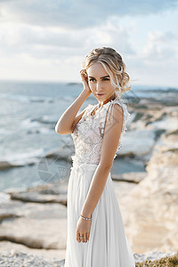 穿着时尚婚纱裸化妆的美丽金发年轻女子模特 在塞浦路斯海岸散步 在塞浦路斯海边行走女士海景金发女郎假期仪式岩石蓝色庆典奢华女性图片
