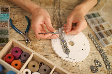 近身的雌性手 用木制桌边的木板 工具 线条 天然石头和彩珠做一个马卡梅手镯 并配有Kumimimio女士纺织品针线活首饰艺术配饰图片