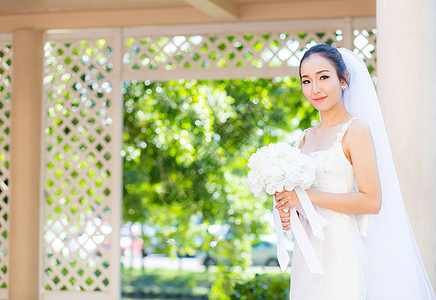 在婚礼当天美丽的年轻女子 穿着白礼服在花园里庆典女孩裙子微笑公园新娘女士头发花束女性图片