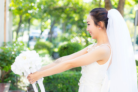 在婚礼当天美丽的年轻女子 穿着白礼服在花园里女性女孩头发裙子庆典微笑公园女士新娘花束图片