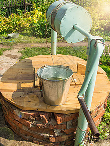 在阳光夏日开张的砖井木盖上的金属桶子图片