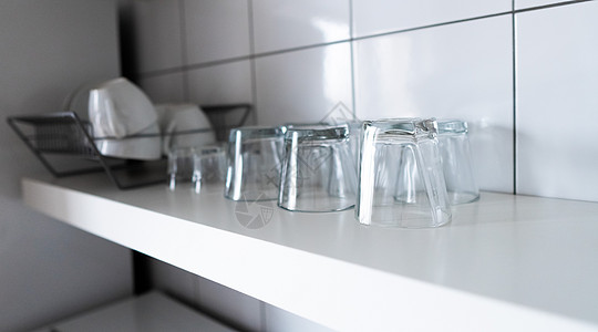 用于存储和展示的宽大厨房搁板和壁架 现代斯堪的纳维亚厨房的白色木架和经济型轻型餐具架 配有餐具 杯子和玻璃杯 贴在墙砖上电器用具图片