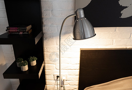 带可调节阅读灯的金属工作灯 在黑白现代卧室的床边 有长臂和不透明灯罩的钢制下桥落地灯 在斯堪的纳维亚内部的时髦的床头灯公寓床头奢背景图片