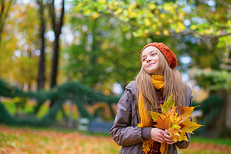 秋天带着一堆叶子的年轻女孩花园绒球橙子帽子快乐围巾城市季节头发女性图片