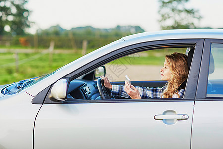 妇女驾驶汽车时使用智能手机司机镜子车辆青少年短信金发女士成功腰带女孩图片