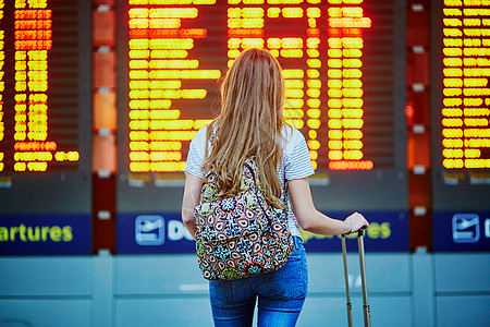 在国际机场 靠近航班信息板 背着背包和行李的旅游女孩旅行学生金发成人线条假期航空公司手提游客滑板车图片