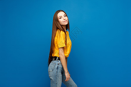 蓝色背景的身穿黄衬衫和牛仔裤 身材瘦弱的模特女孩的侧面视图 与世隔绝图片