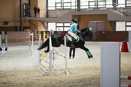 骑着黑马的年轻女性骑手 跳过障碍物图片