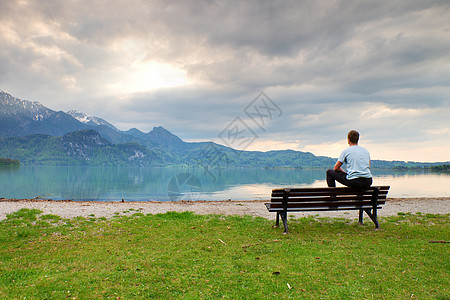 穿蓝衬衫的成年男子在山湖海岸坐在旧木板凳上休息海岸山脉运动员天空头发自由乡愁海洋公园图片
