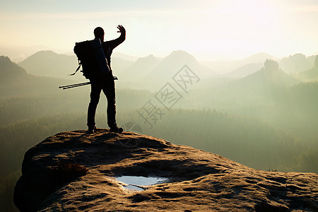 在山顶上打劫 背包机手握有杆子的黑眼 春日破晓岩石活动男生运动小路薄雾登山杖风衣冒险旅行者图片