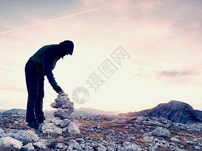 独自一人的成年男子在金字塔上长着石头 阿尔卑斯山峰顶 天亮时日落之夜爬坡兜帽高山登山旅游胜地日出岩石远足峰值回忆图片