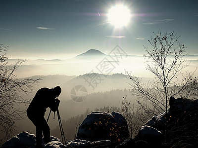 太阳早上 摄影师在三脚架上准备摄像头湿度反转天空粉雪相机橙子阳光职业枝条树干图片