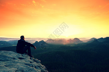 在山上看着橙色黎明的男子爬坡享受远足男人阳光远足者天空地平线夹克冒险图片