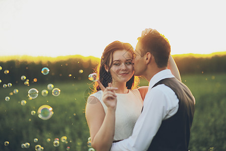 日落时 快乐的新娘和新郎在公园里互相拥抱 肥皂泡沫 婚礼 幸福的爱情概念婚姻气泡夫妻女士白色新人男性天空摄影丈夫图片